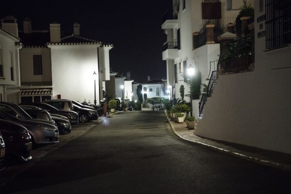 Flera vitkalkade hus ses omge en liten gata med en boendeparkering med bilar på rad. Foto.