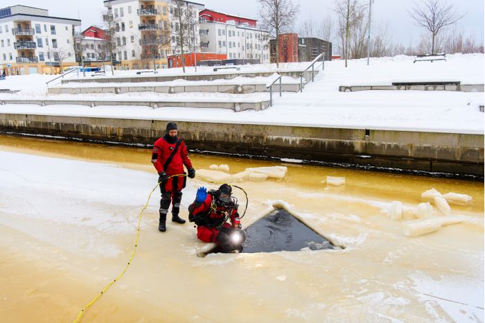 En dykare letar efter ett föremål i en kanal mellan bostadshus. Foto.