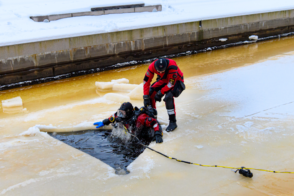Dykaren som varit kvar ovanför is hjälper till att dra upp sin kollega från isvaken. Foto.
