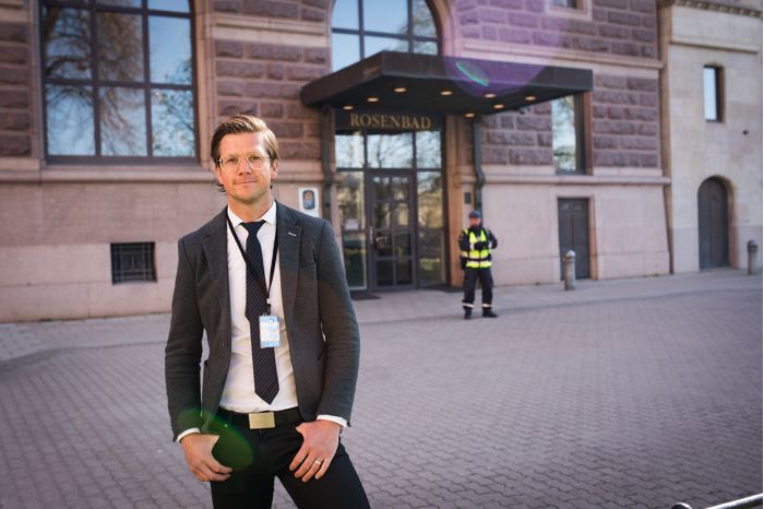 Marcus står framför entrén till Rosenbad. Han bär kostym och har ett passerkort runt halsen.