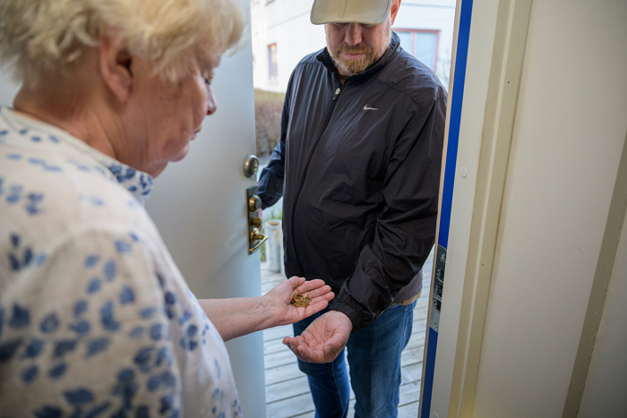 En äldre kvinna är på väg att lägga över en guldkedja i handen på en man med keps som står i dörröppningen. Arrangerad bild.