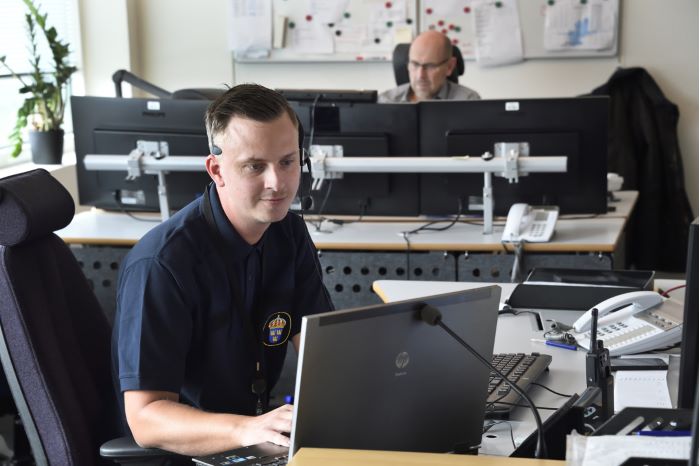 Jimmy Modin, i mörkblå pikétröja med polisemblem, sitter framför sin datorskärm med headset på huvudet.