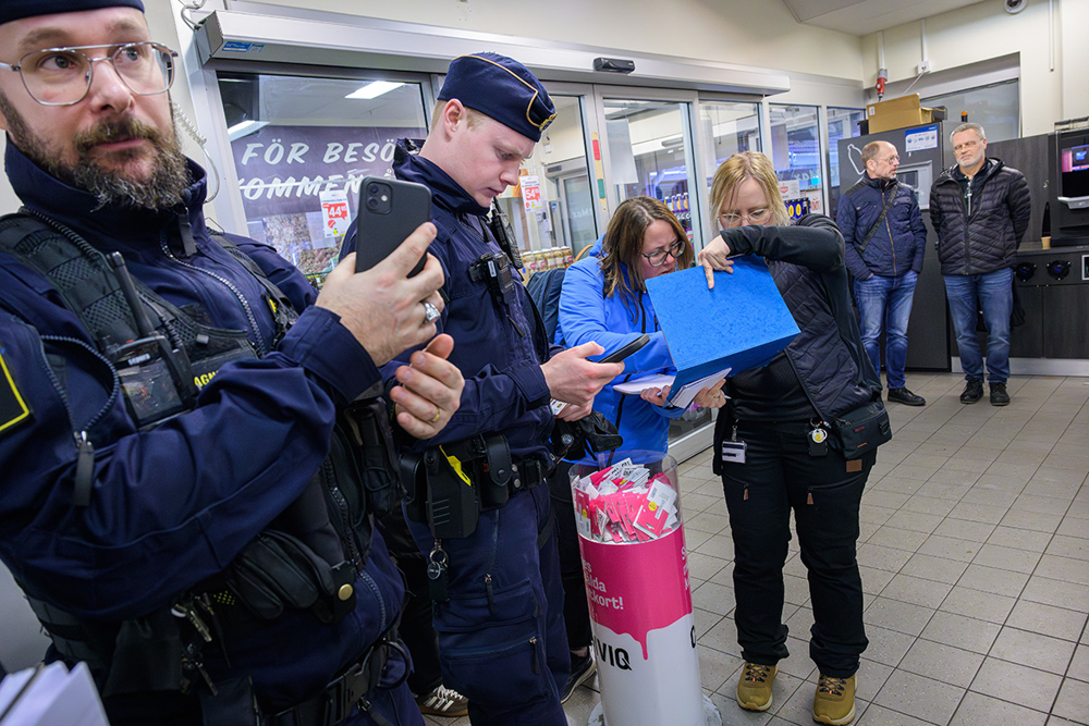 Två gränspoliser står och väntar och i bakgrunden ses inspektörer från andra myndigheter. Foto.