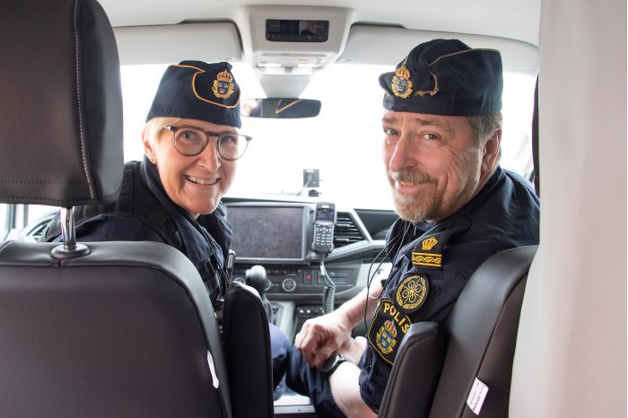 Elisabeth ”Bettan” Samuelsson och Mikael Finsberg sitter i en polisbil tillsammans och tittar bak mot baksätet. Foto.