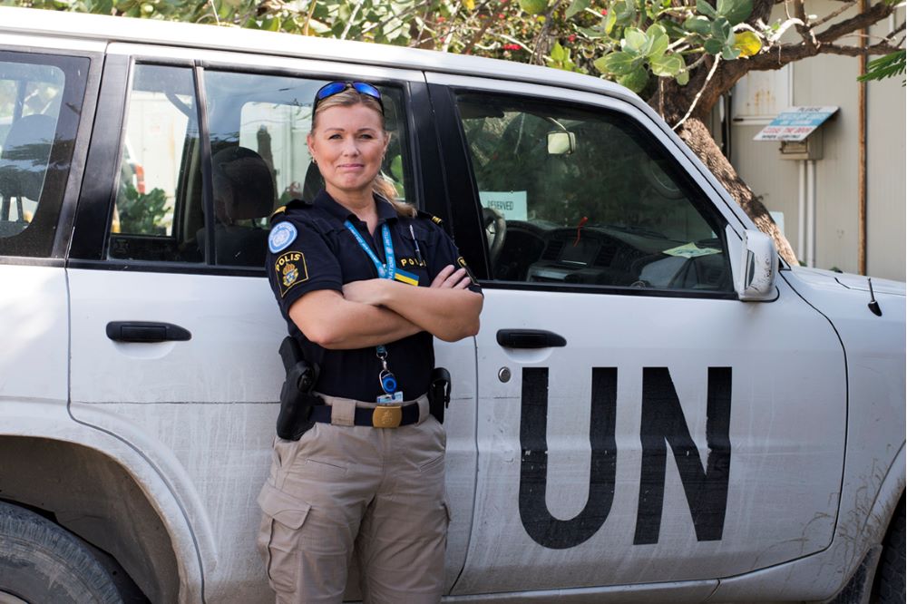 Tutti Blixt står i sin uniform framför en vit FN-bil av jeepmodell.