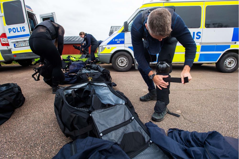 Tre poliser spänner på sig skyddsutrustning. Foto.