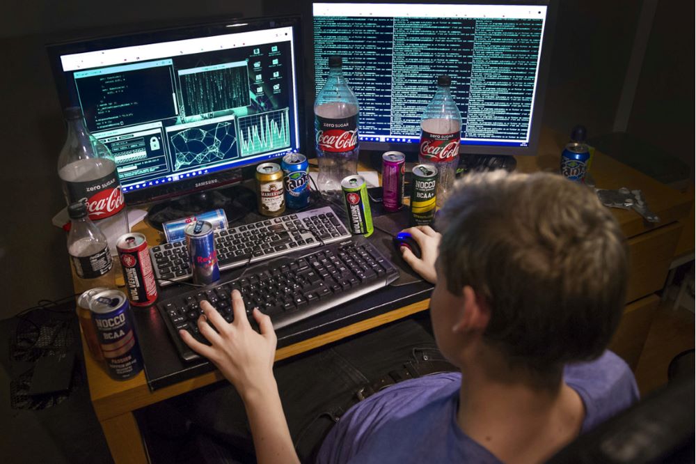 Ung kille sitter framför två datorskärmar vid ett belamrat skrivbord