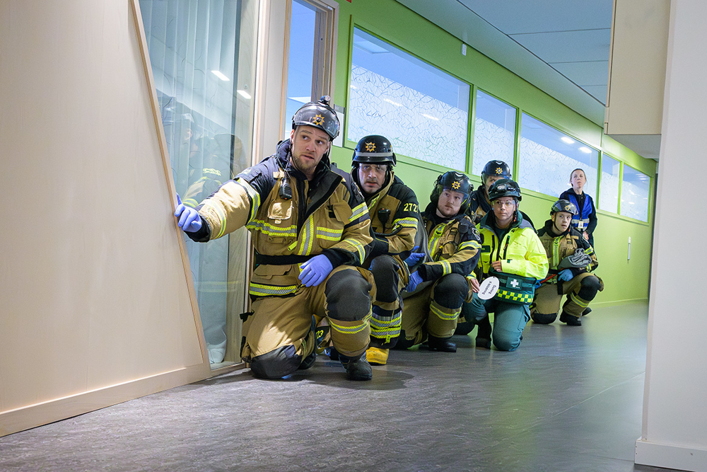 Personal från räddningstjänst och ambulans sitter på huk och väntar på att få gå vidare in och börja rädda liv. Foto.