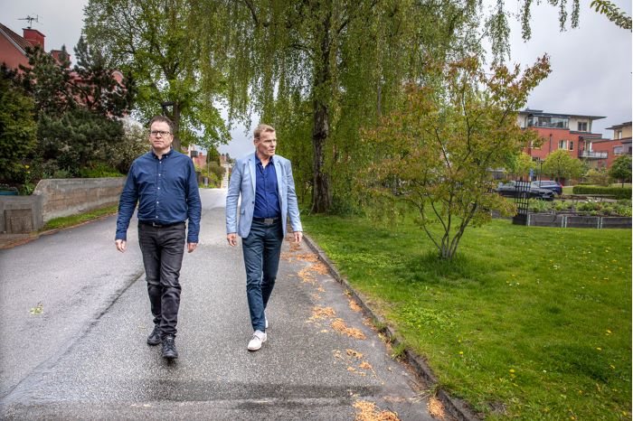 Släktforskaren Peter Sjölund och utredningsledaren Jan Staaf går på en asfalterad gata i ett bostadsområde. Foto.