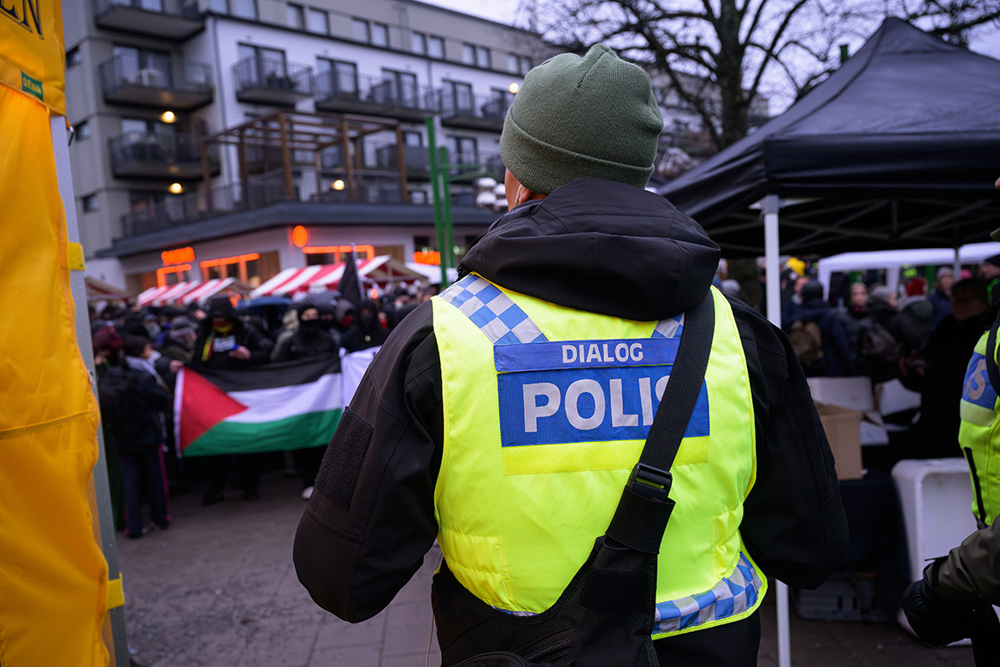 Ryggen på en polis med gul väst där det står: "Dialogpolis". Foto.