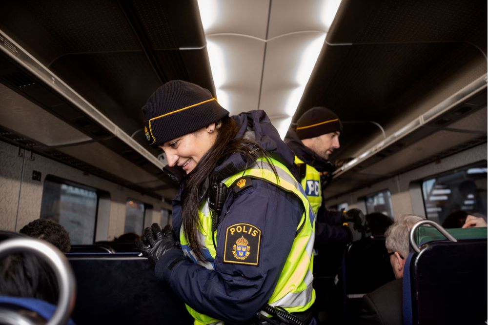 Kvinnlig uniformerad polis kontrollerar id-handlingar i tågvagn.
