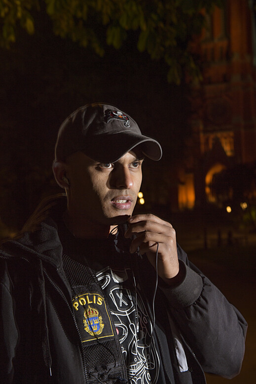 Simon Häggström pratar in i mikrofonen på sina mobilhörlurar utomhus i mörkret. Foto.