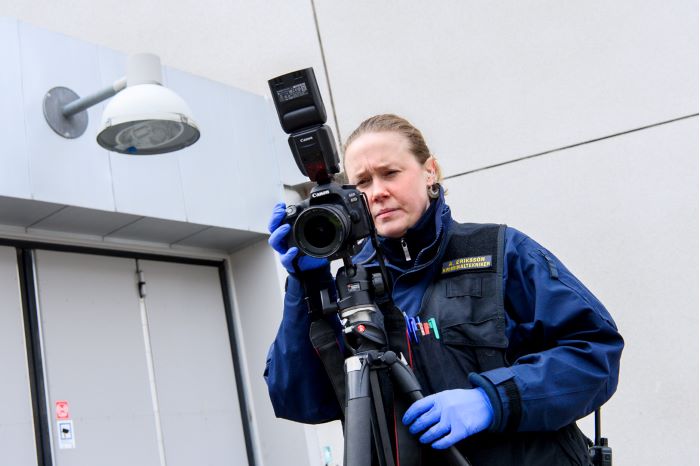 Annelie Eriksson står bakom sin kamera på stativ för att ta bilder av brottsplatsen. Foto.