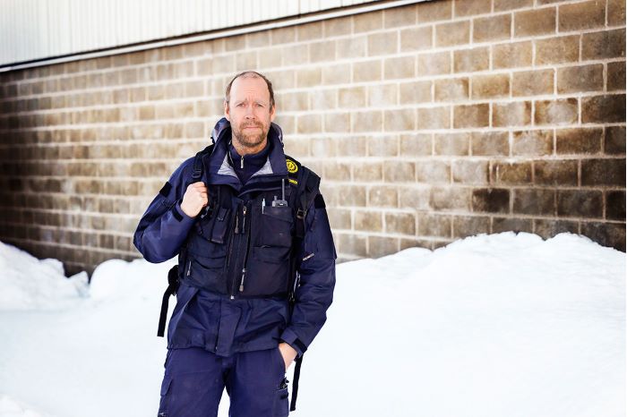 Johan Engman står i sina arbetskläder utomhus på snöbeklädd mark. Foto.