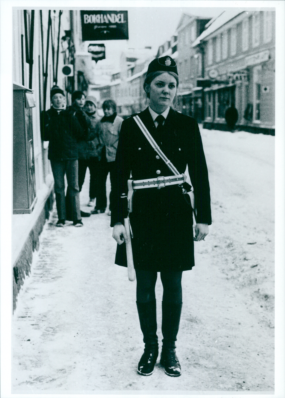 En kvinnlig polis i polisuniform med poliskjol, beväpnad med vit batong. Foto.