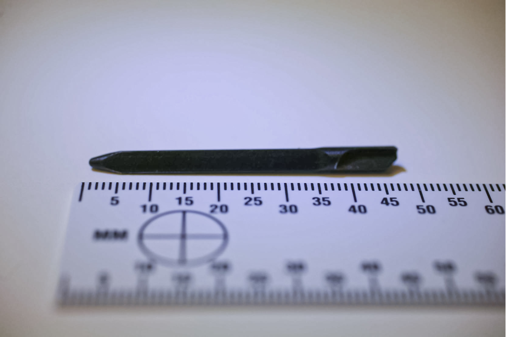 Ett slagstift som ser ut som en liten metallpinne ligger framför en linjal och mäter under 5 cm. Foto