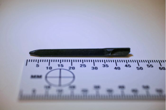 Ett slagstift som ser ut som en liten metallpinne ligger framför en linjal och mäter under 5 cm. Foto