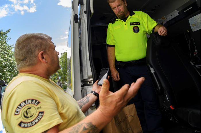 Bilinspektör står i polisbil pratar med en man som håller sin mobil i handen.