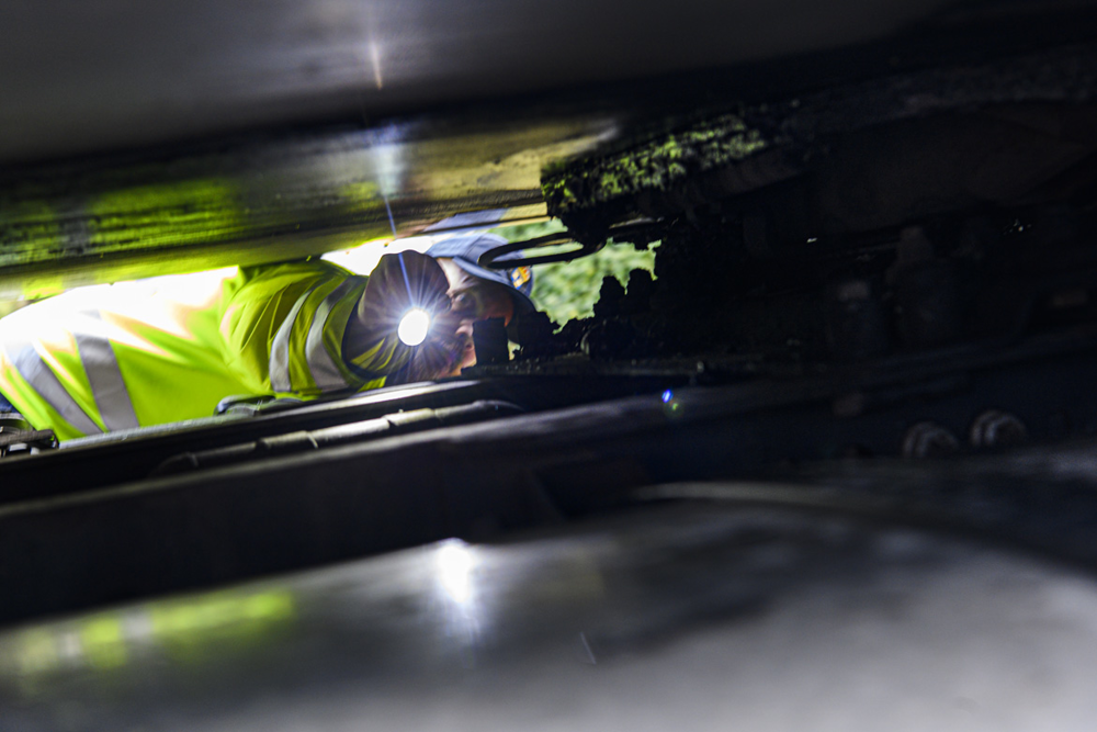 Man med reflexjacka lyser med ficklampa in under en lastbil.