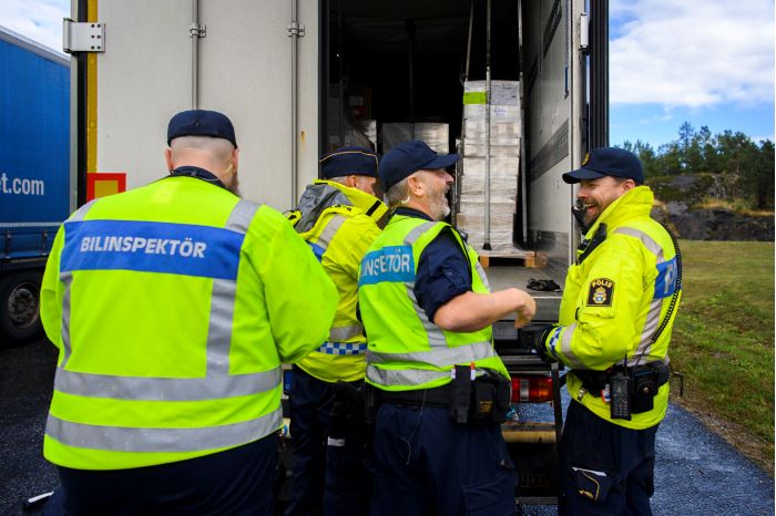 Två bilinspektörer och två poliser står bakom en lastbil. Två av dem skrattar.