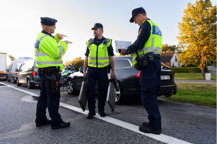 Tre poliser står framför en svart bil och pratar.