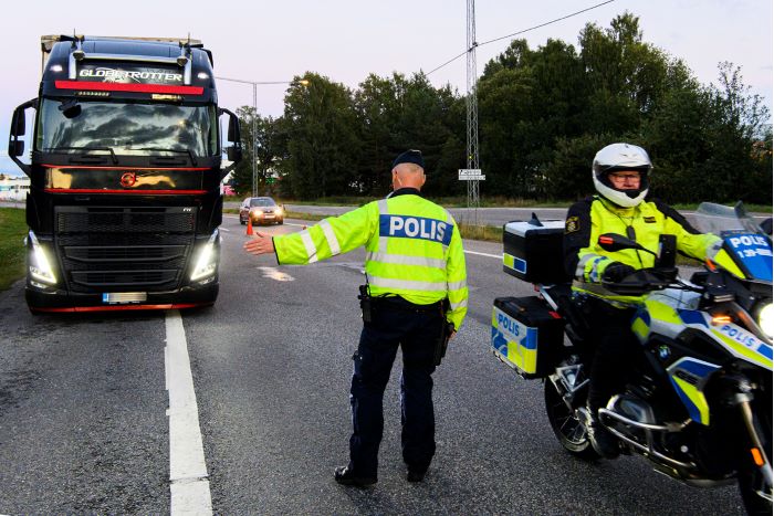 Polis vinkar in en lastbil till vägkanten. Framför står en polismotorcykel.