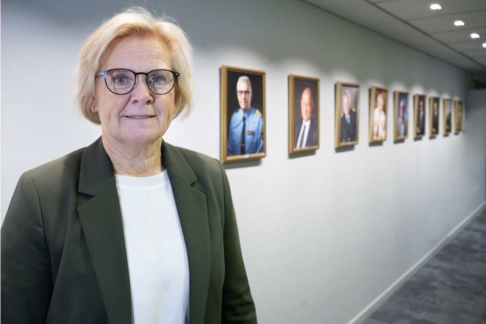 Petra Lundh står framför raden av porträtt över tidigare rikspolischefer. Foto.