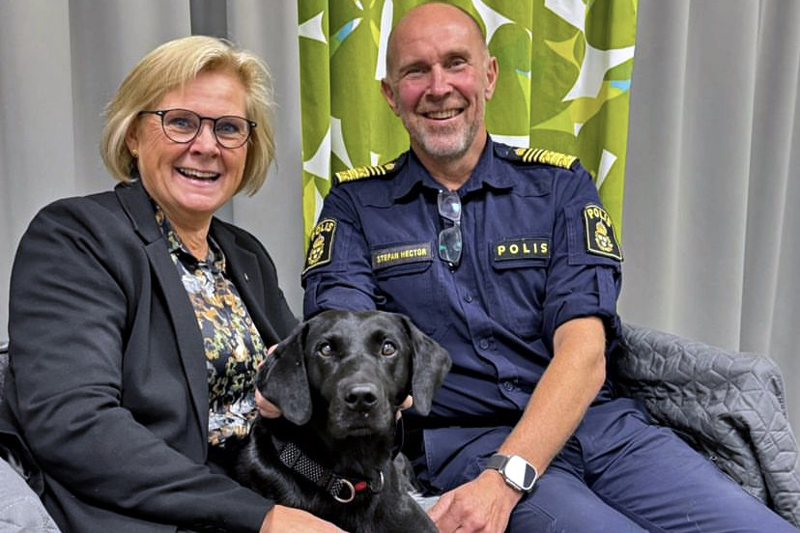 Petra Lundh och Stefan Hector med en svart labrador mellan sig i en soffa. Foto.