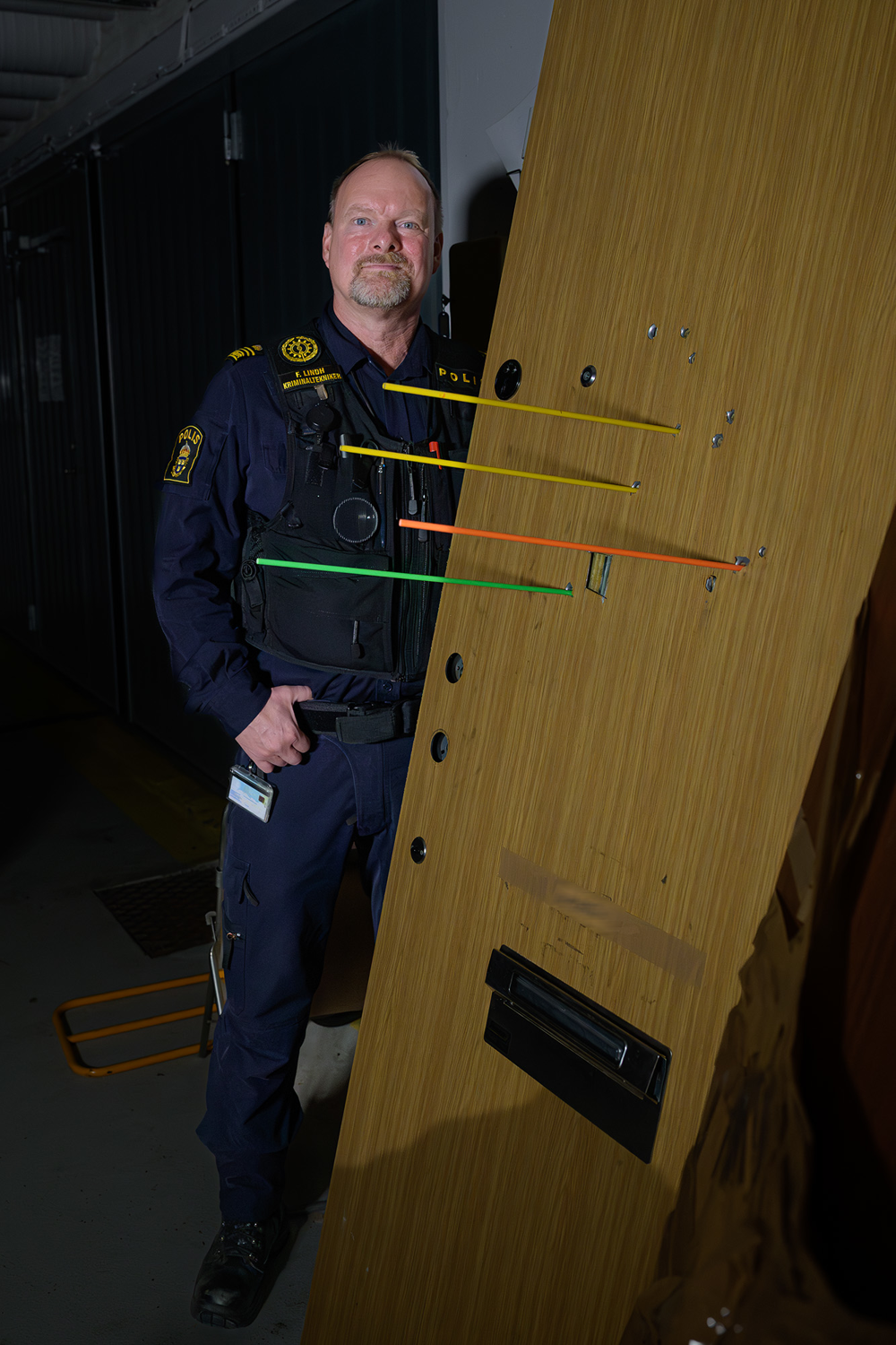 Fredrik Multing Lindh står bredvid en nedtagen ytterdörr som har flera kulhål i sig. Foto. 