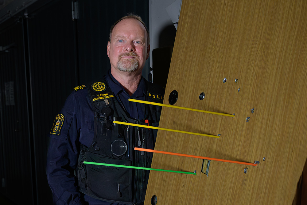 Fredrik Multing Lindh står bredvid en nedtagen ytterdörr som har flera kulhål i sig. Foto. 