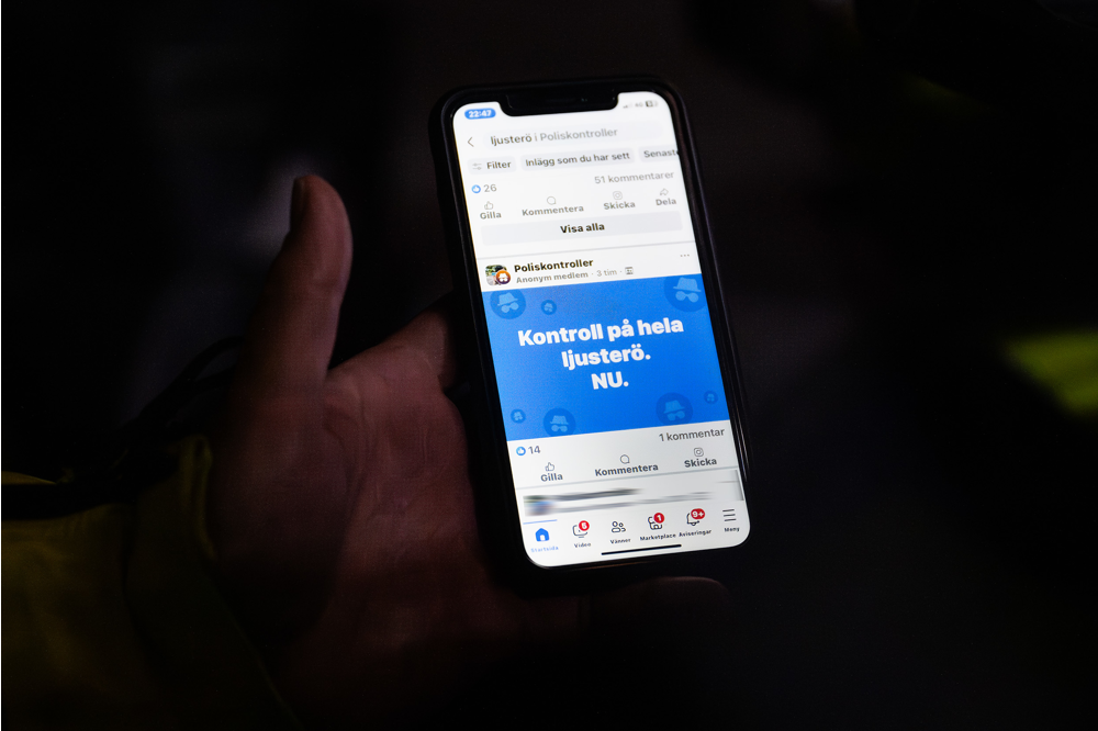 En mobiltelefon hålls upp där man kan läsa meddelandet: "Kontroll på hela Ljusterö. NU." Foto.