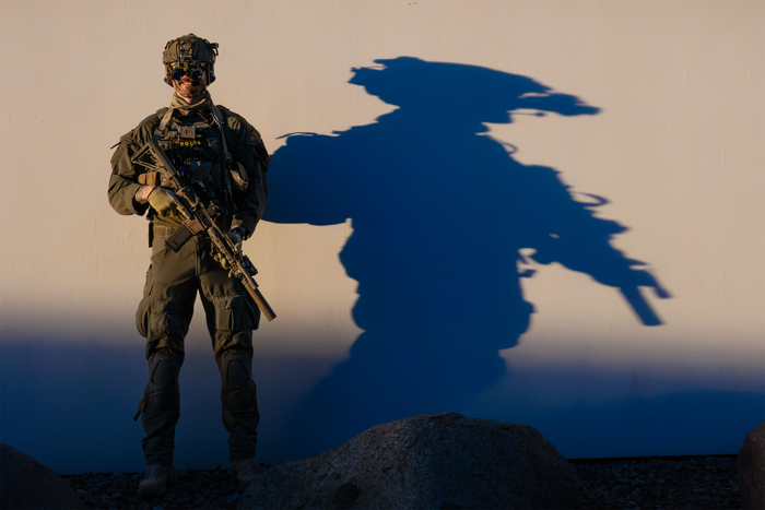 En operatör står med sitt vapen framför en vägg och en skugga kastas mot väggen. Foto.
