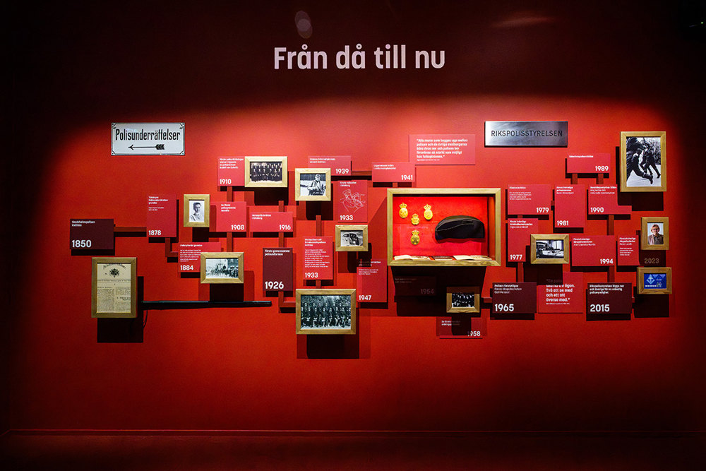 En rödmålad vägg med foton, årtal och berättande texter. Foto.