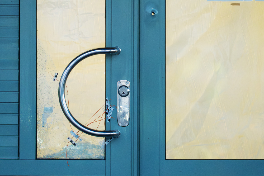 En blå entrédörr med skotthål i sig, där glasrutorna är täckta med papp. Foto.