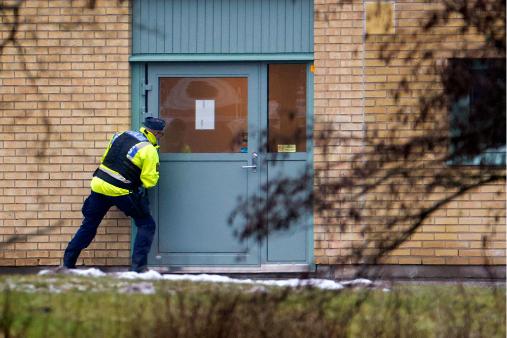 En polis ses försiktigt spana in genom rutan på en av entrédörrarna till Risbergska. Foto.