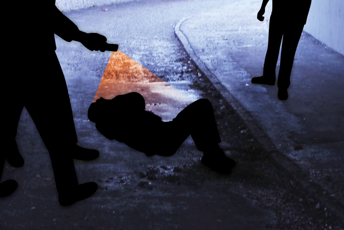 Siluetter av en man som ligger ner på asfalten medan en person filmar och en står bredvid. Illustration.