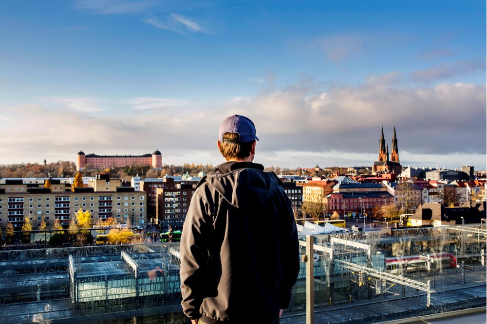 Anders Nilsson står med ryggen mot kameran, på en terass med glasräcke och blickar ut över Resecentrum i Uppsala