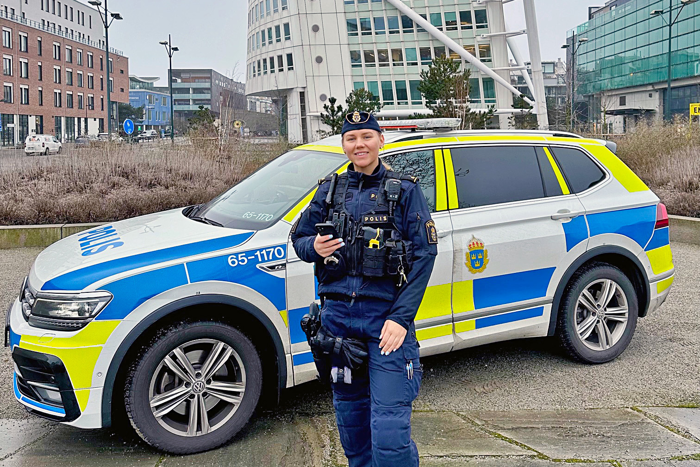 Polisen och sociala medier-samordnaren Ellen Halldin står framför en polisbil i Malmö med Turning Torso i bakgrunden. Foto.