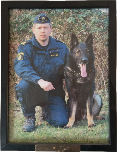 Niklas Wilsson i polisuniform sitter på knä med sin hund Jocky bredvid honom. Foto.