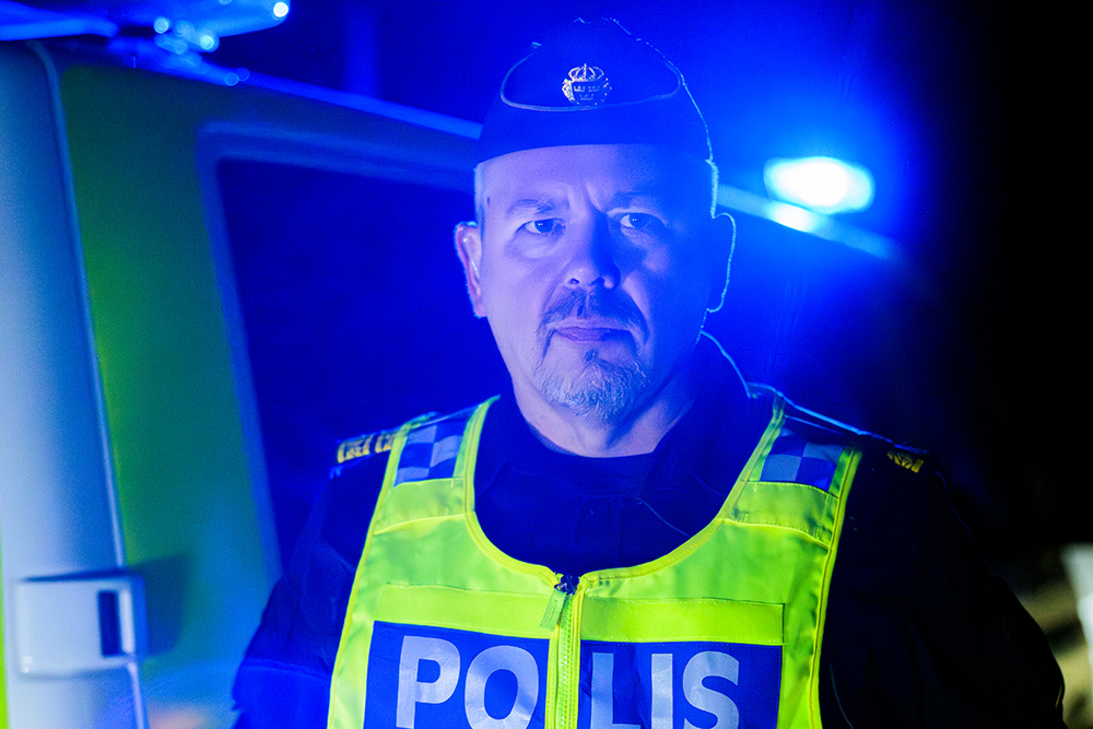 Niklas Wilsson, chef för polisområde Kalmar och Kronoberg, står utomhus på kvällen i skenet av blåljus. Foto.
