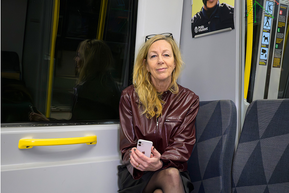 Sofia Halling, grafisk formgivare och AD, sitter på en stol i tunnelbanan. Ovanför huvudet syns en affisch där det står "Polisliv". Foto.