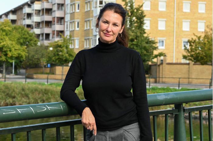 Susanne Gosenius står på en bro med lägenhetshus i bakgrunden. Foto.