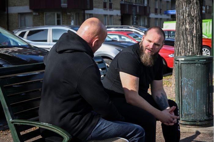 Förhandlaren Kent sitter  med den föreställda hotaktören (figurant) på en parkbänk och pratar. Foto.