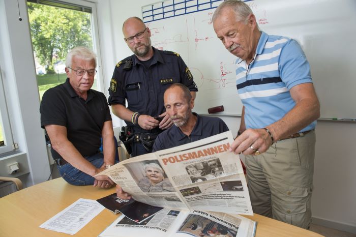 Fyra poliser, varav en i uniform, bläddrar i gamla tidningar vid ett skrivbord.