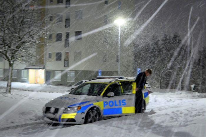 En polisbil står på snöig liten gata och en polis ses kliva ur bilen i snöstormen. Foto.