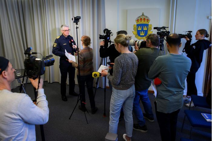 Rikspolischefen håller presskonferens framför reportrar med kameror. Foto.