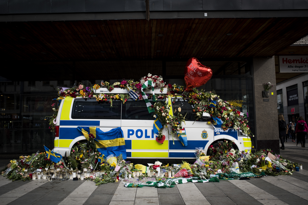 En polisbuss täckt av blommor och ytterligare blombuketter ligger runtom. Foto.