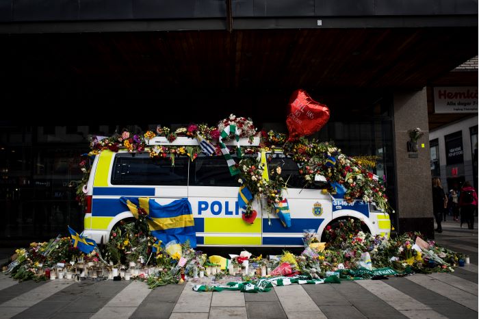 En polisbuss täckt av blommor och ytterligare blombuketter ligger runtom. Foto.
