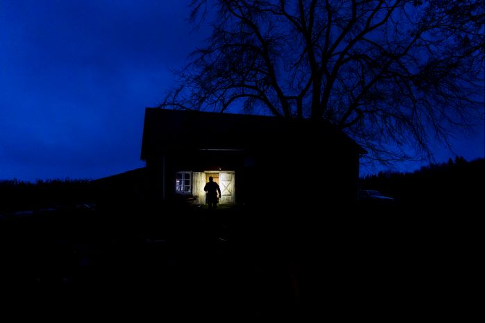 Siluetten av en polis när hen ska gå in i ett hus som står svart mot den mörka himlen. Foto.