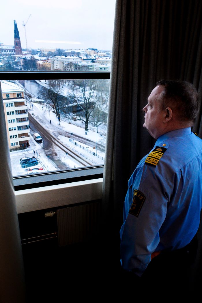 Polisområdeschef Pär Halldén står och tittar ut genom ett fönster, där man ser ett snöbeklätt område med flerfamiljshus och en väg. Foto.